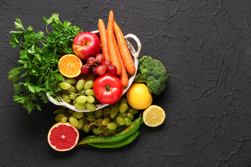 Wicker basket with different fresh fruits and vegetables on black background