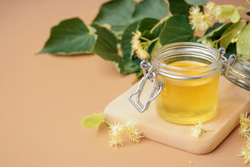 Wooden board with jar of linden honey on brown background