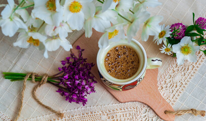 Obraz na płótnie Canvas Coffee with foam and spring wildflowers on a white tablecloth.