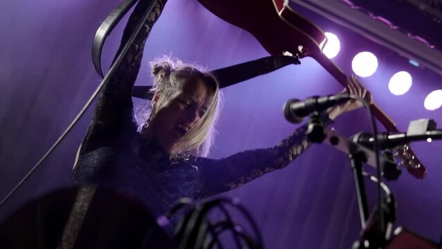 Closeup of an excited Professional guitarist singing, screaming and performing in night club lights close up. Attractive hot girl singer dancing, jumping with guitar, hands in the air and having fun