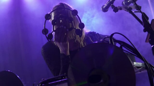 Close-up portrait of the Caucasian blonde singer performing on stage in nightclub lights with her face behind the half moon tambourine. A confident, talented woman singing song with the microphone. 