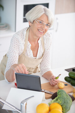 senior woman cooking with help of recipe on tablet