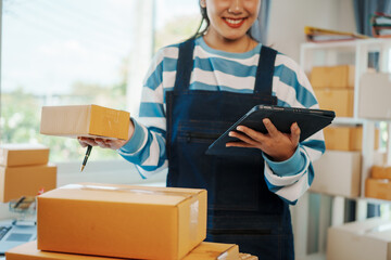 Startup small business SME of independent Asian woman wearing apron using laptop and boxes to...