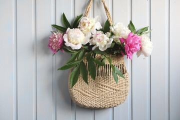 A bouquet of peonies in a woven bag on a white background.