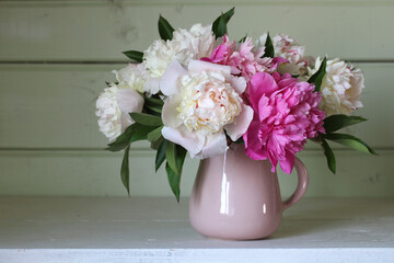 A bouquet of pink and white peonies on the table in a rural house.