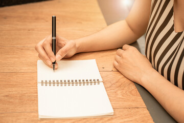 Woman hand is writing on a blank notepad with a pen on wood background.