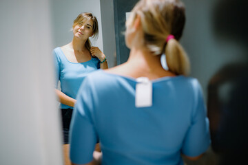 Elegant customer trying on new t-shirt in dressing room. Woman touching hair, tilting head and admiring reflection.