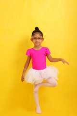 4 year old brunette Latina girl with glasses dressed in a pink leotard and white tutu takes her...
