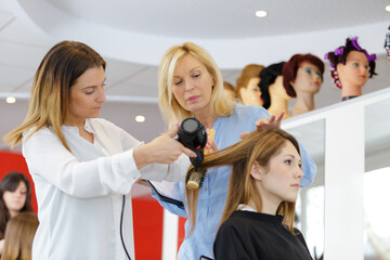 trainee hairdresser blow drying female customers hair