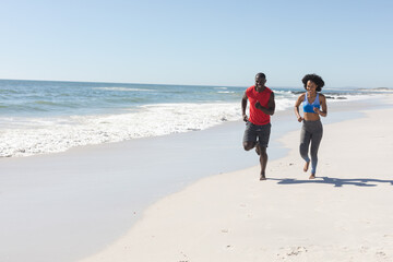 Happy, fit african american couple exercising, running on sunny beach