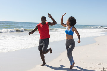 Happy, fit african american couple exercising, running and high fiving on sunny beach