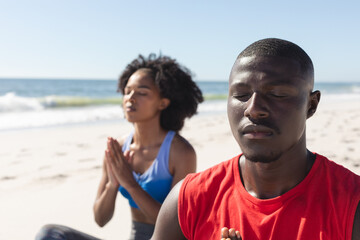 Happy, fit african american couple practicing yoga meditation sitting on sunny beach