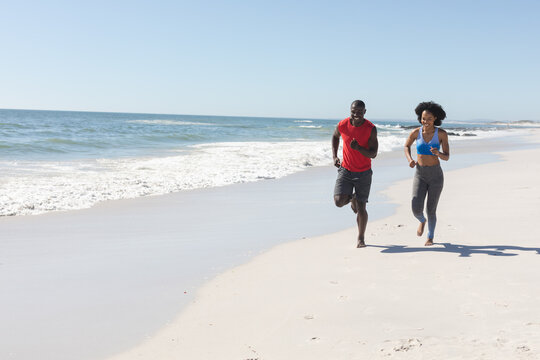 Happy, fit african american couple exercising, running on sunny beach