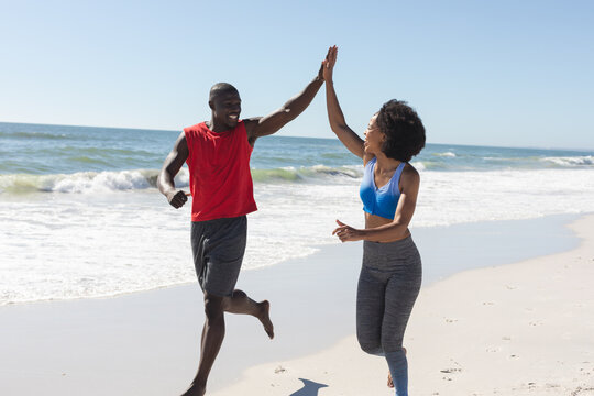 Happy, fit african american couple exercising, running and high fiving on sunny beach