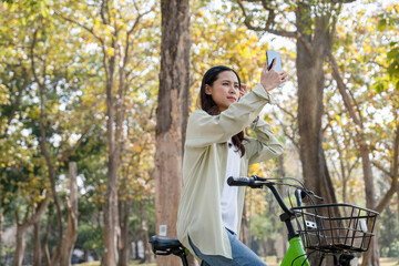 Happy woman riding bicycle and taking selfie at park.