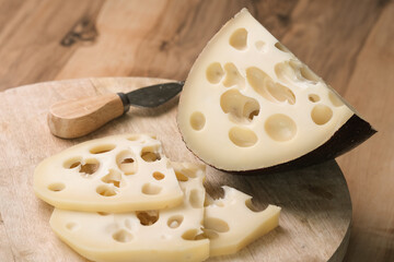 Emmental cheese triangle, Swiss cheese, on wooden board whith knife and craft bag. High resolution image