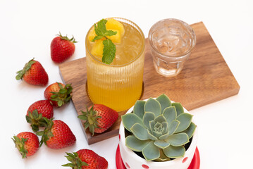 mango juice in a glass on a wooden page with strawberries on the side