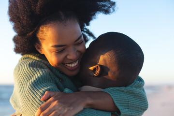 Happy african american couple embracing and smiling on sunny beach