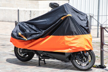 motorbike orange black protected by plastic cover in street motorcycle with tarpaulin jacket