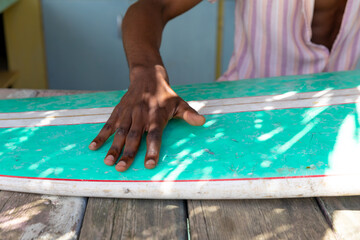 Midsection of african american man preparing surfboard behind counter of surf hire beach shack