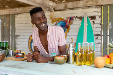 Happy african american male bartender smiling behind the counter at beach bar