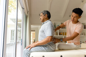 Diverse male physiotherapist and senior male patient massaging back