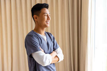 Profile of happy asian male doctor against beige curtain with copy space