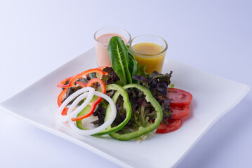 Vegetable salad with green, red bell peppers, onions, large slices with cos, green oats, tomatoes, with two kinds of dressing on a white plate, on a white background