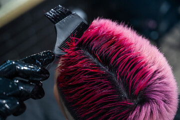 Close-up of the process. The hairdresser dyes the hair of an Asian woman in pink. Short extreme haircut.  - obrazy, fototapety, plakaty