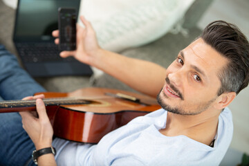 man using phone while playing guitar