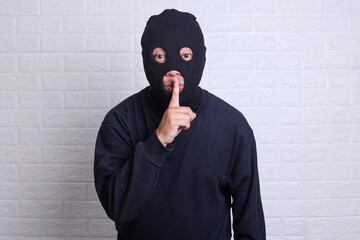 Thief in a mask showing sign quieter isolated on white background