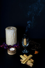 burning palo santo in a glass cup accompanied by white lighted candles and a Tibetan mala