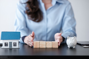 Close up Asian women's hand with 4 wooden block and wooden house model on the table for business, finance, saving money and property investment concept.