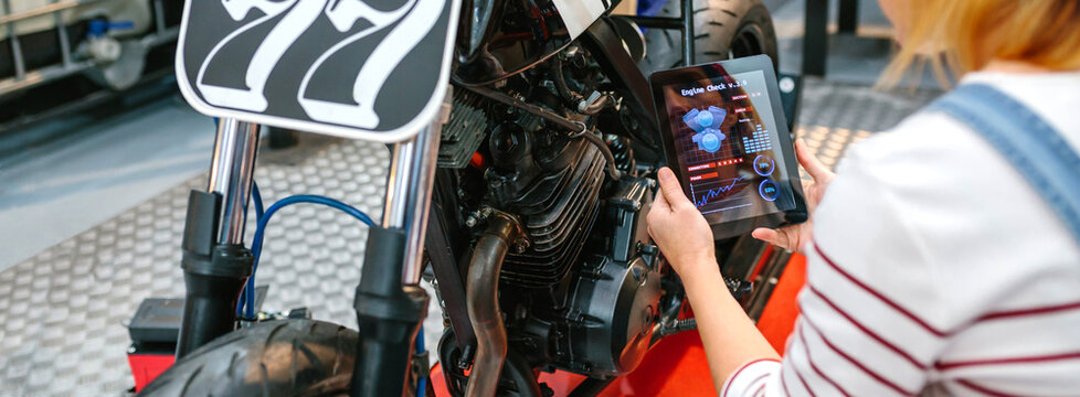 Unrecognizable mechanic woman using a diagnosis app in digital tablet to review custom motorcycle on factory