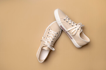 Beige fabric sneakers on brown background flat lay top view. Fashion sneakers, casual sports shoes with laces. Stylish summer spring sneakers, minimalistic footwear background with copy space