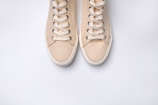 Beige fabric sneakers on white background flat lay top view. Fashion sneakers, casual sports shoes with laces. Stylish sneakers, minimalistic footwear background with copy space