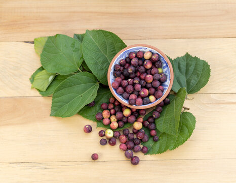 Grewia asiatica falsa fruit in a clay bowl with green leaves on a wooden background. Selective focus with top view