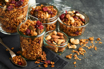 Homemade granola in glass jar with greek yogurt or milk and cashews, almonds, pumpkin with dried cranberry seeds in dark grey table background. Healthy energy breakfast or snack. Top view