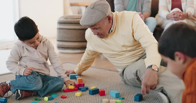 Family, building blocks and a grandfather playing with his grandchildren in the home living room during a visit. Kids, love or toys with a male grandparent bonding with his boy grandkids on the floor