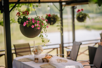 in the close-up, a flower pot hangs on the edge of the terrace, in the background a decorated table under the terrace