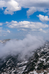 Obraz premium Beautiful landscape from the top of a dark rocky mountain covered with snow on a sunny day. Blue sky and clouds in background. Alps mountain top in Austria. Powerful, wild, nature scenery. 