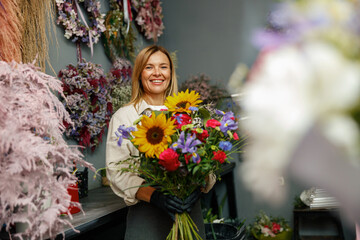 Woman florist smiling and holding beautiful flowers composition in flower shop ready to sale 