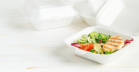 Healthy lunch box with salad and grilled chicken on white wooden background. 