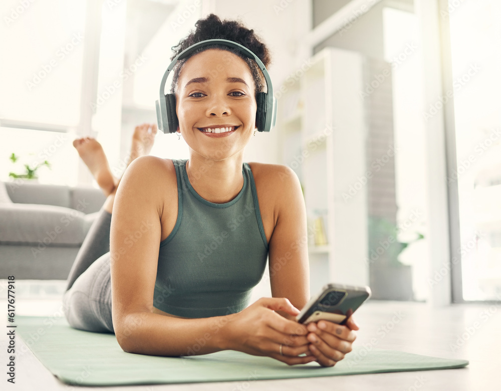 Wall mural Yoga, portrait and happy woman relax on a living room floor with music, headphones and phone for streaming at home. Face, smile and lady on fitness break with social media, radio or podcast in lounge