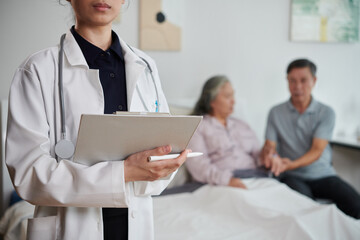 Cropped image of serious family doctor standing in bedroom of sick senior woman and her husband