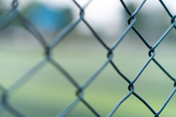 Fototapeta premium Cells of braided metal fence installed on border of private property preventing penetration of unwanted guests on blurred background protective steel grid