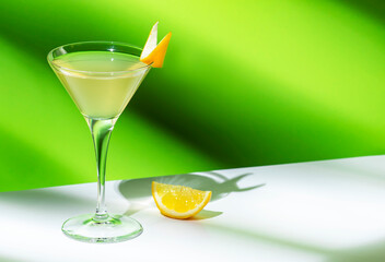 Vesper cocktail drink with dry gin, vodka, aperitif, lemon zest and ice in martini glass. Light green background, hard light, shadow pattern