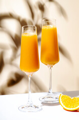 Mimosa summer cocktail drink with orange juice and cold dry champagne or sparkling wine in glasses. Beige background, hard light, shadow pattern