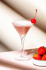 Bounty martini summer cocktail drink with vodka, liqueur, cream, strawberries and ice in glass with red cocktail cherry. Beige pink background