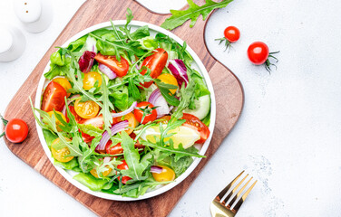 Fresh vegan vegetable salad with colorful tomatoes, cucumber, red onion, lettuce and arugula. White table background, top view